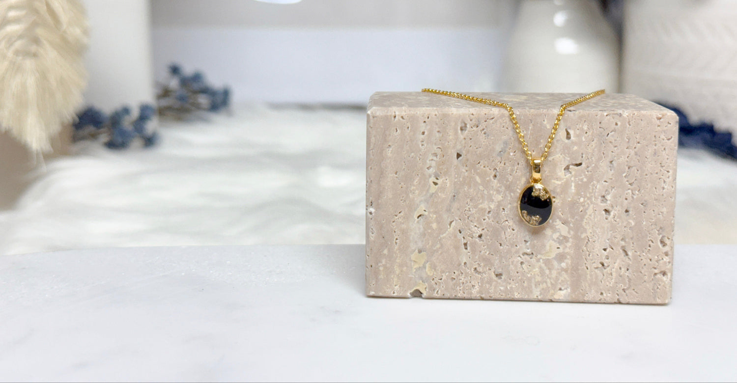 The Elena Necklace featuring a gold solitaire oval pendant with a black breastmilk stone and gold flakes, creating a unique and meaningful keepsake.